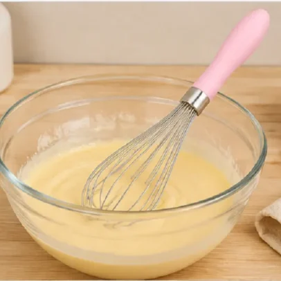 Stainless steel balloon whisk with pink ergonomic handle for egg beating baking and kitchen mixing.,
